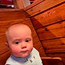 baby, child, infant, wooden_booth, restaurant, indoor, face, person, sitting, clothing, shorts, arm, head, eyes, skin, seat, furniture, light, expression, casual
