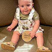 Colsen is registered to the contest to win money with this photo: baby, child, infant, sitting, couch, overalls, sandals, wooden_sign, smiling, happy, indoors, cute, clothing, face, person, light, shadow, skin, eyes, hand