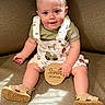 baby, child, infant, sitting, couch, overalls, sandals, wooden_sign, smiling, happy, indoors, cute, clothing, face, person, light, shadow, skin, eyes, hand