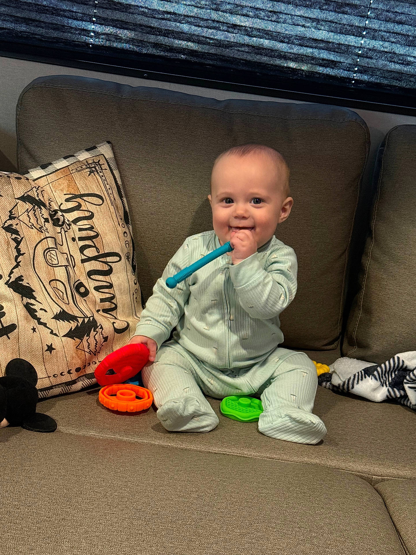 Colsen is registered to the contest to win money with this photo: baby, blanket, chewing, child, colorful, comfortable, couch, cute, decor, happy, indoor, infant, onesie, person, pillow, playtime, seated, smiling, soft_lighting, toys