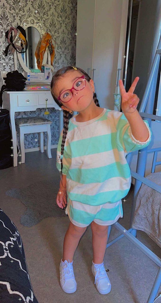 Neyla a rejoint le concours — aidez-le/la à gagner de superbes lots ! baby_toddler_clothing, chair, child, eyewear, flooring, fun, gesture, glasses, goggles, joint, person, personal_protective_equipment, shoulder, sleeve, smile, standing, sunglasses, t_shirt, thumb, toddler