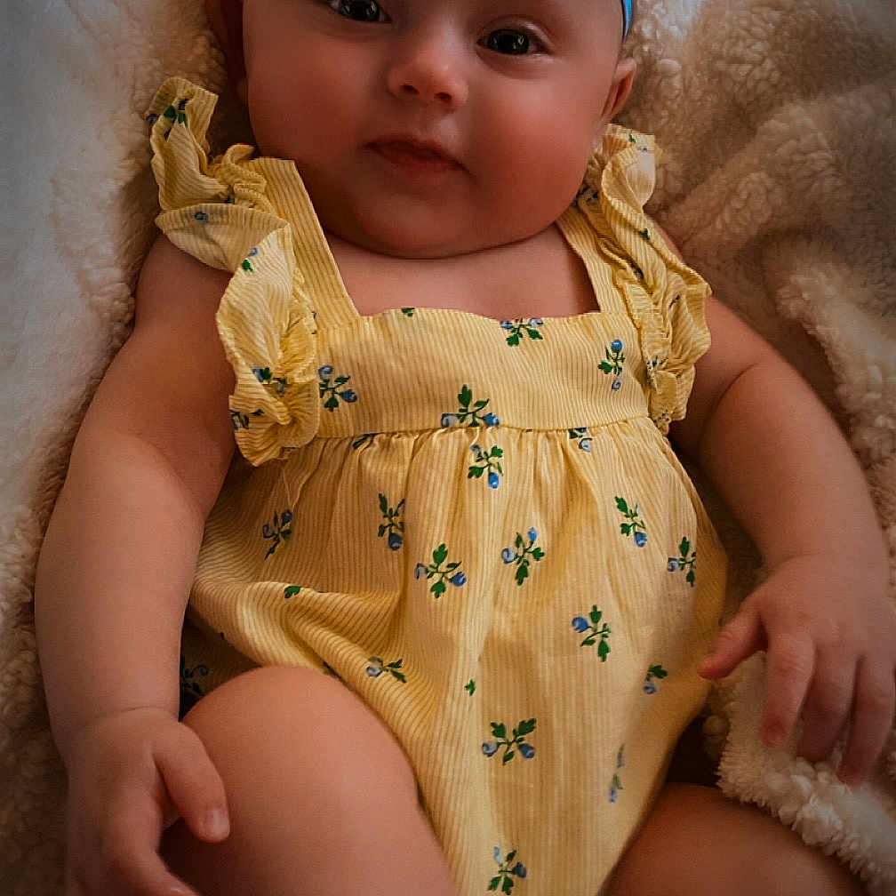 Chloie is registered to the contest to win money with this photo: baby, blanket, blue_headband, bow, child, comfortable, cute, expression, floral_pattern, foot, hand, indoors, infant, person, portrait, romper, sitting, skin, soft_texture, yellow_clothing