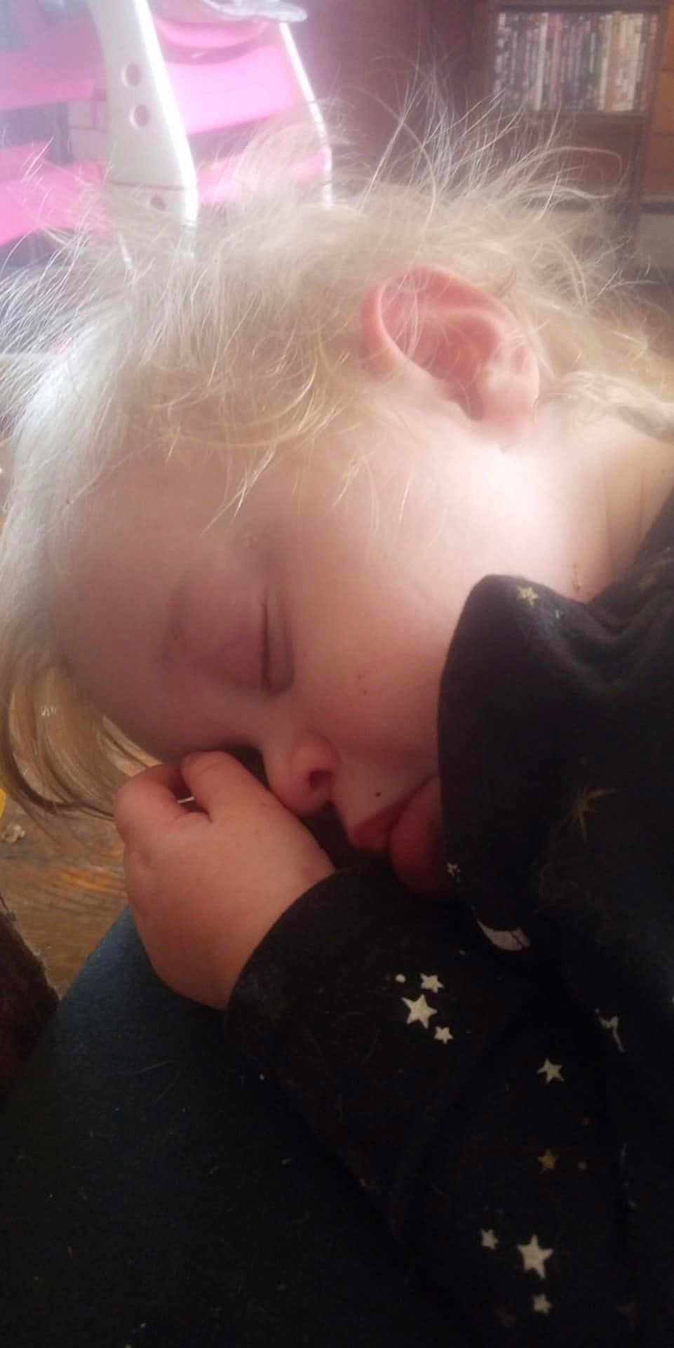 Keira is registered to the contest to win money with this photo: child, sleeping, blond_hair, hand, face, black_clothing, stars_pattern, indoor, furniture, chair, bookshelf, peaceful, portrait, close_up, hair, skin, cozy, rest, nap, young