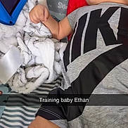 Ethan is registered to the contest to win money with this photo: baby, child, tablet, screen, blanket, pillow, striped_bed, clothing, nike, person, indoor, lying_down, watching, animation, cartoon, soft_toys, bed, cute, infant, relaxed