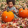 autumn_leaves, casual_clothing, child, curly_hair, cute, daylight, fall, fun, grass, happy, leaf, nature, orange, outdoor, playful, pumpkin, seasonal, sitting, smiling, toddler
