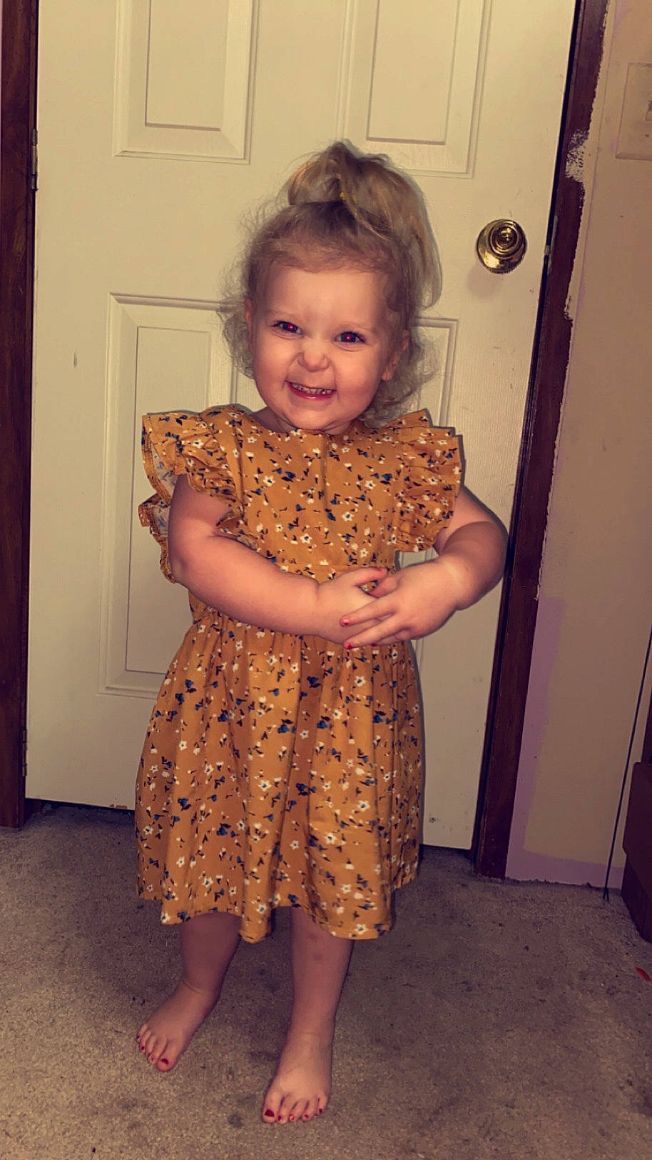 Paisley is registered to the contest to win money with this photo: child, door, dress, fawn, flooring, fun, hair, head, human_body, human_leg, joy, neck, one_piece_garment, pattern, person, sleeve, smile, standing, toddler, trunk
