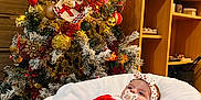 Mélyanah participe au concours pour gagner de l'argent avec cette photo : baby, christmas_tree, christmas_decorations, red_clothing, pacifier, headband, cushion, holiday_stockings, indoor, festive, holiday, smiling, person, furniture, wooden_shelf, lights, ornaments, celebration, cozy, child