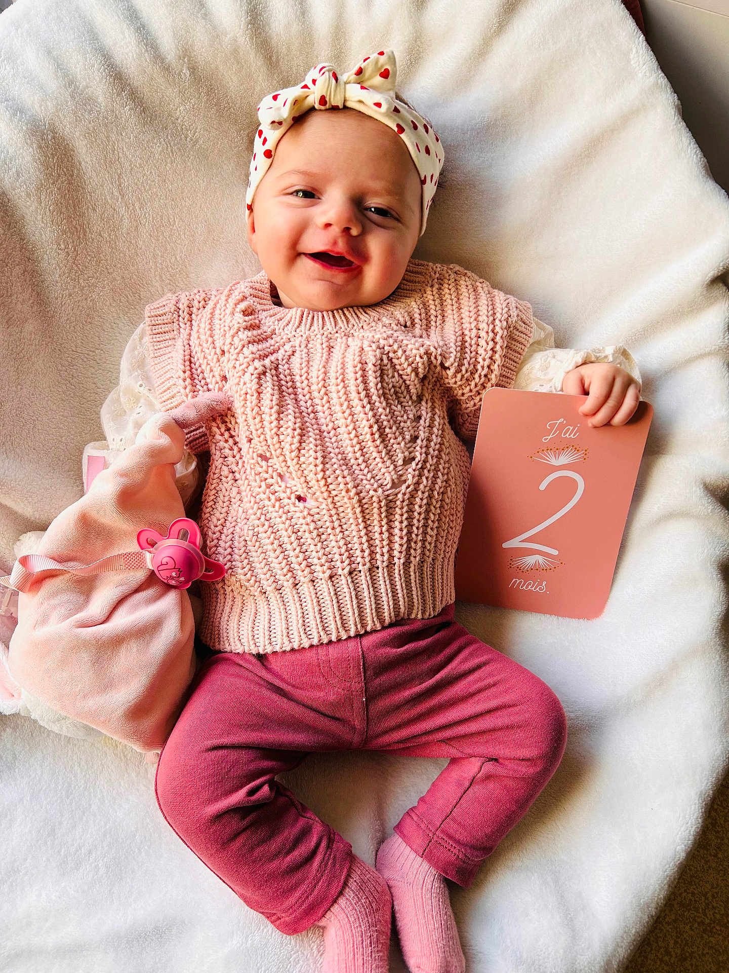 Mélyanah a rejoint le concours — aidez-le/la à gagner de superbes lots ! baby, smiling, infant, pink_clothing, headband, pacifier, milestone_card, blanket, soft_texture, lying_down, cute, cozy, child, happy, indoors, knitwear, socks, portrait, two_months, accessory