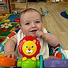 Declan joined the competition — help win amazing prizes! baby, child, toy, activity_center, lion_toy, colorful, smiling, indoor, playroom, floor, wooden_floor, sitting, infant, face, hand, eyes, clothing, furniture, background, happy