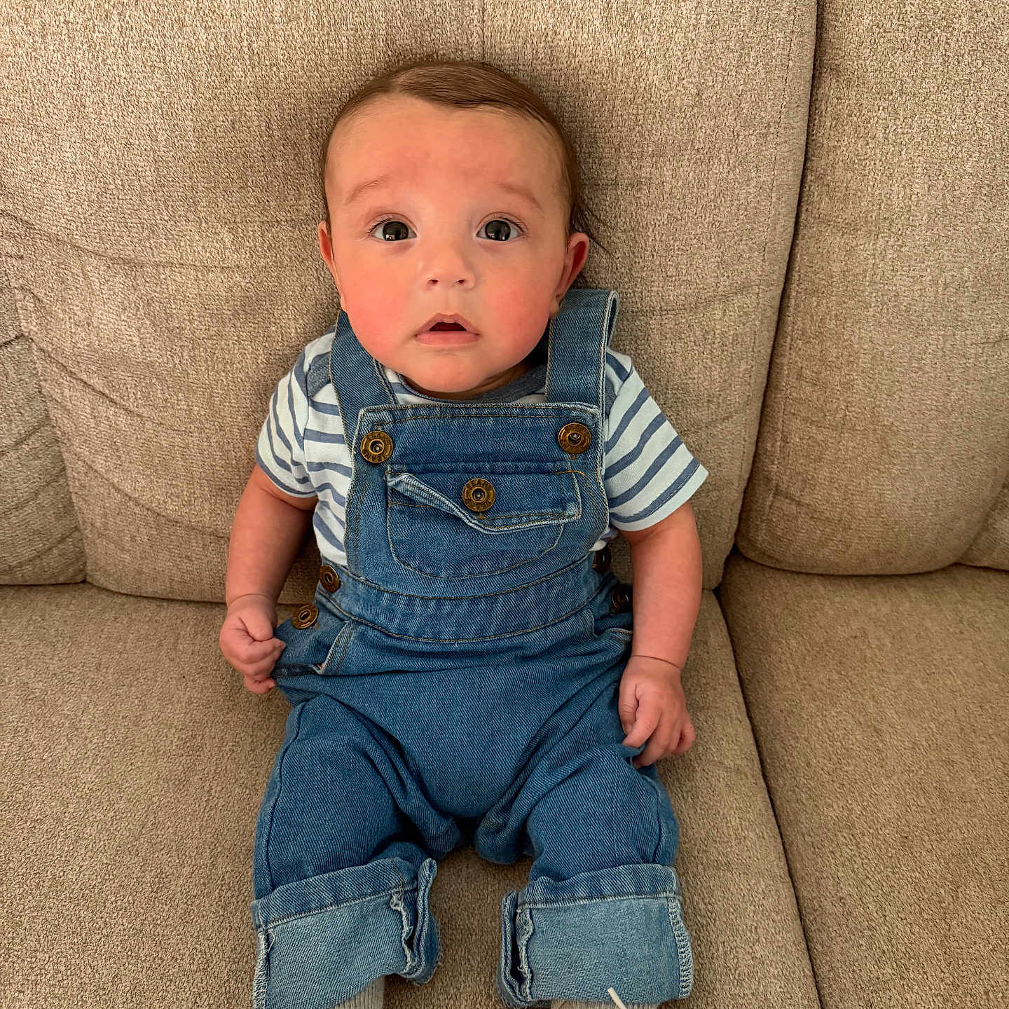 Malachi is registered to the contest to win money with this photo: baby, beige, casual_clothing, child, couch, curious_expression, cute, denim_overalls, eyes, face, fashion, footwear, indoors, infant, portrait, seated, small_hands, striped_shirt, white_shoes, young_child