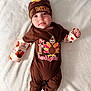 baby, infant, thanksgiving, holiday, brown_clothing, hat, onesie, turkey_graphic, white_blanket, cute, smiling, portrait, child, feet, hand, lying_down, festive, soft_texture, celebration, indoors