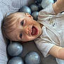 baby, child, smiling, blue_eyes, ball_pit, gray_balls, playful, happy, face, mouth_open, infant, clothing, short_sleeve, skin, head, cute, lying_down, indoors, person, joyful