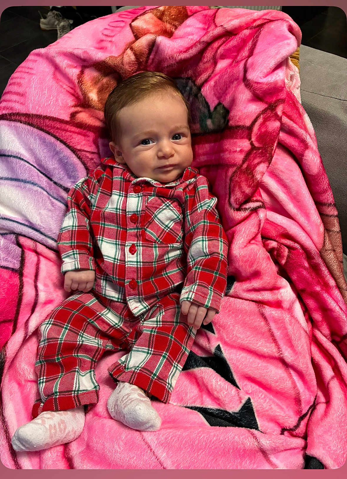 Romy participe au concours pour gagner de l'argent avec cette photo : baby, infant, plaid_pajamas, red, white, blanket, pink, socks, face, portrait, indoors, cute, child, clothing, person, resting, soft, fabric, couch, expression