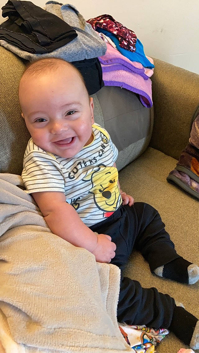 Jake is registered to the contest to win money with this photo: baby, baby_toddler_clothing, cheek, child, comfort, couch, flooring, happy, human_leg, joy, knee, lap, leg, person, sitting, skin, sleeve, smile, t_shirt, thigh