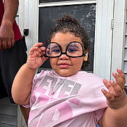 Lilth is registered to the contest to win money with this photo: adult_arm, casual_clothing, child, curly_hair, door, expression, funny_glasses, glasses, hand, home, necklace, outdoor, person, pink_shirt, playful, portrait, screen_door, smile, toddler