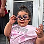 adult_arm, casual_clothing, child, curly_hair, door, expression, funny_glasses, glasses, hand, home, necklace, outdoor, person, pink_shirt, playful, portrait, screen_door, smile, toddler