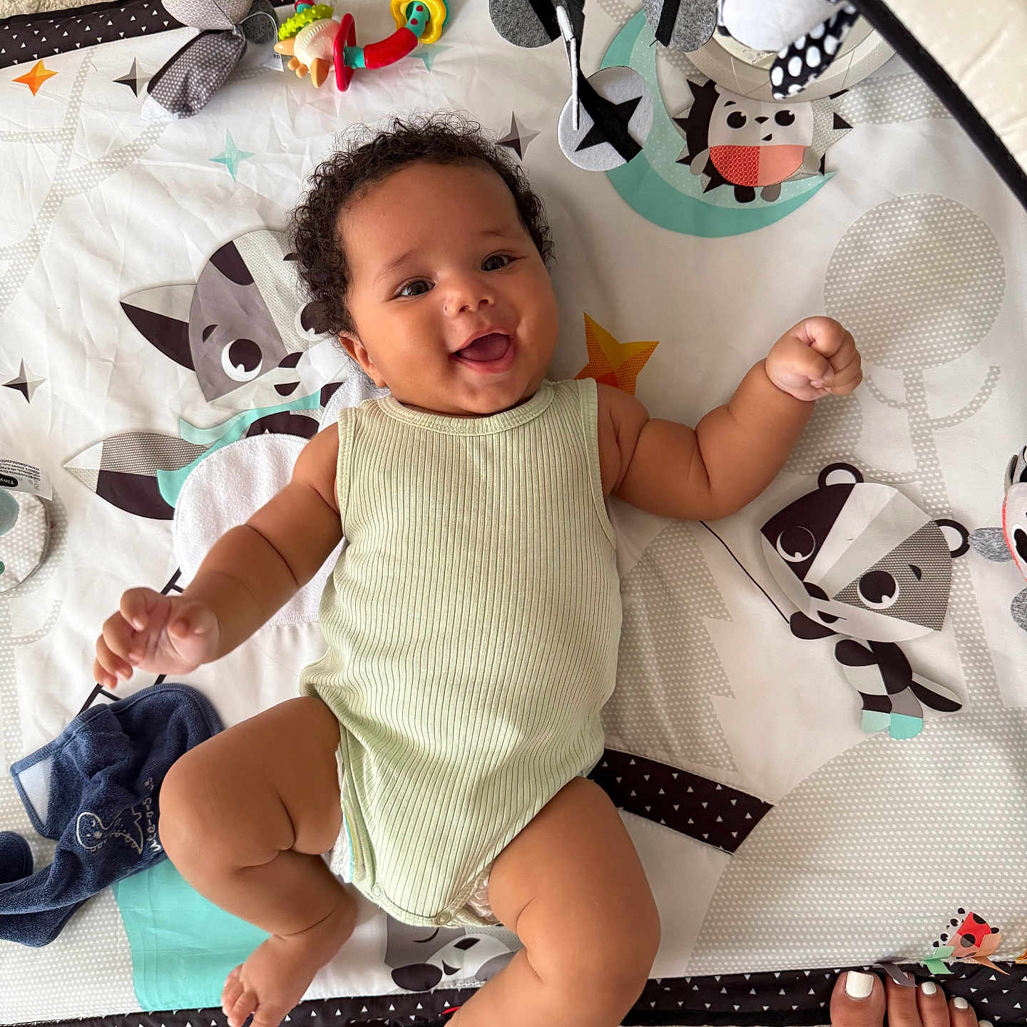 Aïnis participe au concours pour gagner de l'argent avec cette photo : animal_patterns, baby, carpet, child, chubby_arms, chubby_legs, clothing, colorful, cute, happy, indoors, infant, lying_down, nail_polish, play_mat, sleeveless_onesie, smiling, soft, toes, toy