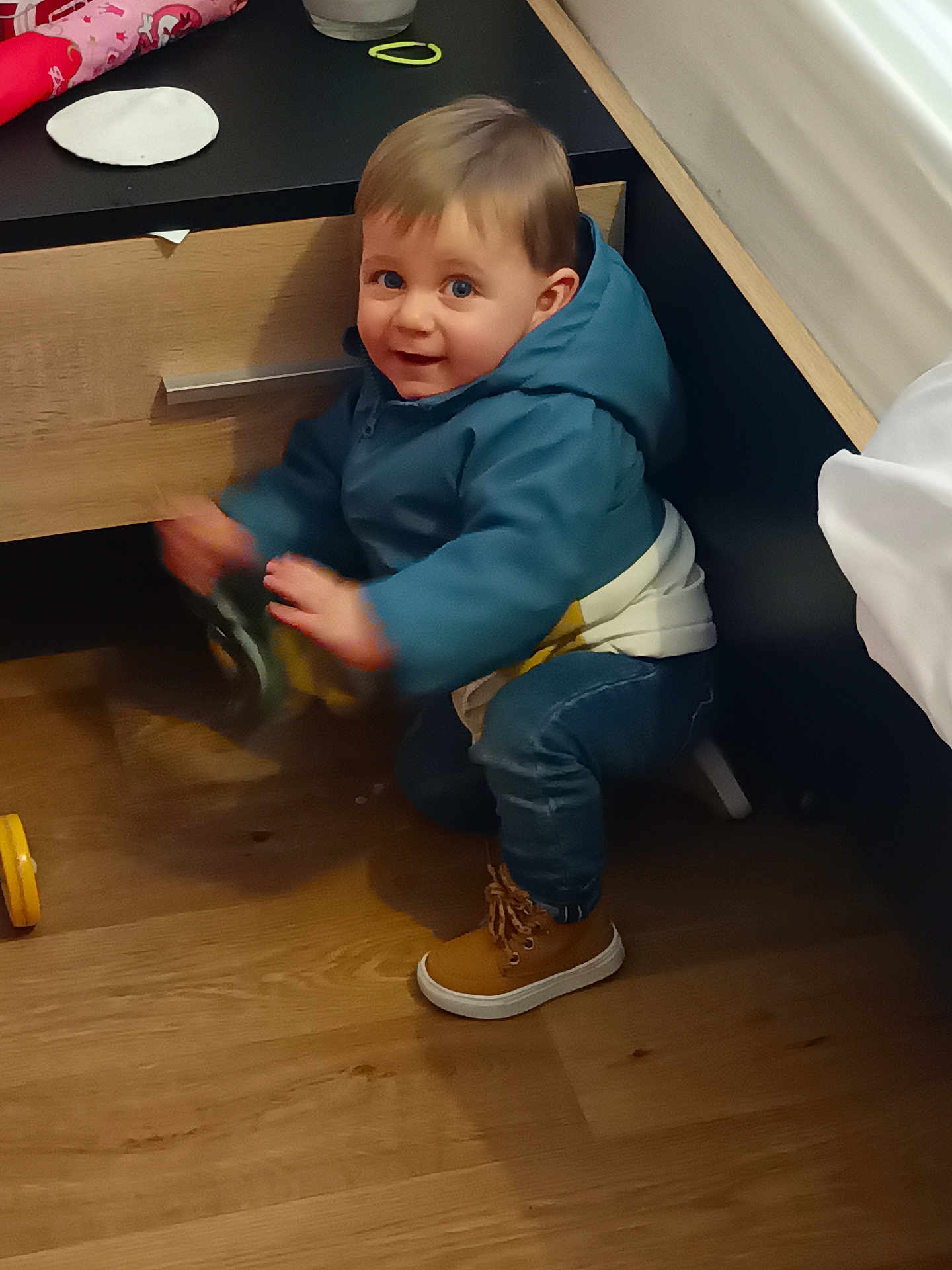 Taho participe au concours pour gagner de l'argent avec cette photo : toddler, child, indoor, blue_jacket, brown_boots, toy, wooden_floor, drawer, bed, curious, happy, playing, squatting, person, clothing, furniture, young_child, motion_blur, smile, hair
