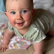 Penelope is registered to the contest to win money with this photo: baby, child, crawling, blue_eyes, rosy_cheeks, blanket, cushion, indoor, person, smiling, infant, cute, soft_lighting, short_hair, green_clothing, homedecor, portrait, close_up, happy, toddler