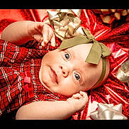 Sage is registered to the contest to win money with this photo: baby, infant, child, red_clothing, plaid, headband, bow, gift_wrapping, silver_bow, holiday, festive, portrait, cute, smiling, face, hands, blue_eyes, lying_down, celebration, closeup