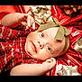 baby, infant, child, red_clothing, plaid, headband, bow, gift_wrapping, silver_bow, holiday, festive, portrait, cute, smiling, face, hands, blue_eyes, lying_down, celebration, closeup