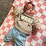 Sage is registered to the contest to win money with this photo: baby, infant, blanket, pink, white, checkered, sweater, clothing, headband, pacifier, floor, carpet, child, person, cute, lying_down, blue_pants, socks, indoors, portrait
