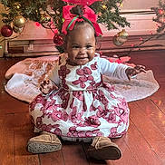 Zaylee is registered to the contest to win money with this photo: baby, child, smiling, christmas_tree, holiday, dress, red_bow, floor, wooden_floor, decorations, ornaments, festive, cute, happy, indoor, celebration, holiday_lighting, person, toddler, seasonal