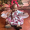 baby, child, smiling, christmas_tree, holiday, dress, red_bow, floor, wooden_floor, decorations, ornaments, festive, cute, happy, indoor, celebration, holiday_lighting, person, toddler, seasonal