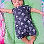 baby, infant, lying_down, romper, palm_tree_pattern, green_cushion, bed, colorful_bedding, child, cute, indoors, sleepwear, person, small_child, soft_lighting, relaxed, skin, foot, hand, head