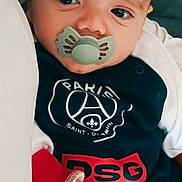 Cristiano participe au concours pour gagner de l'argent avec cette photo : baby, pacifier, infant, clothing, face, hand, portrait, close_up, indoor, child, cute, person, young, soft_lighting, expression, newborn, bed, sleepwear, logo, resting