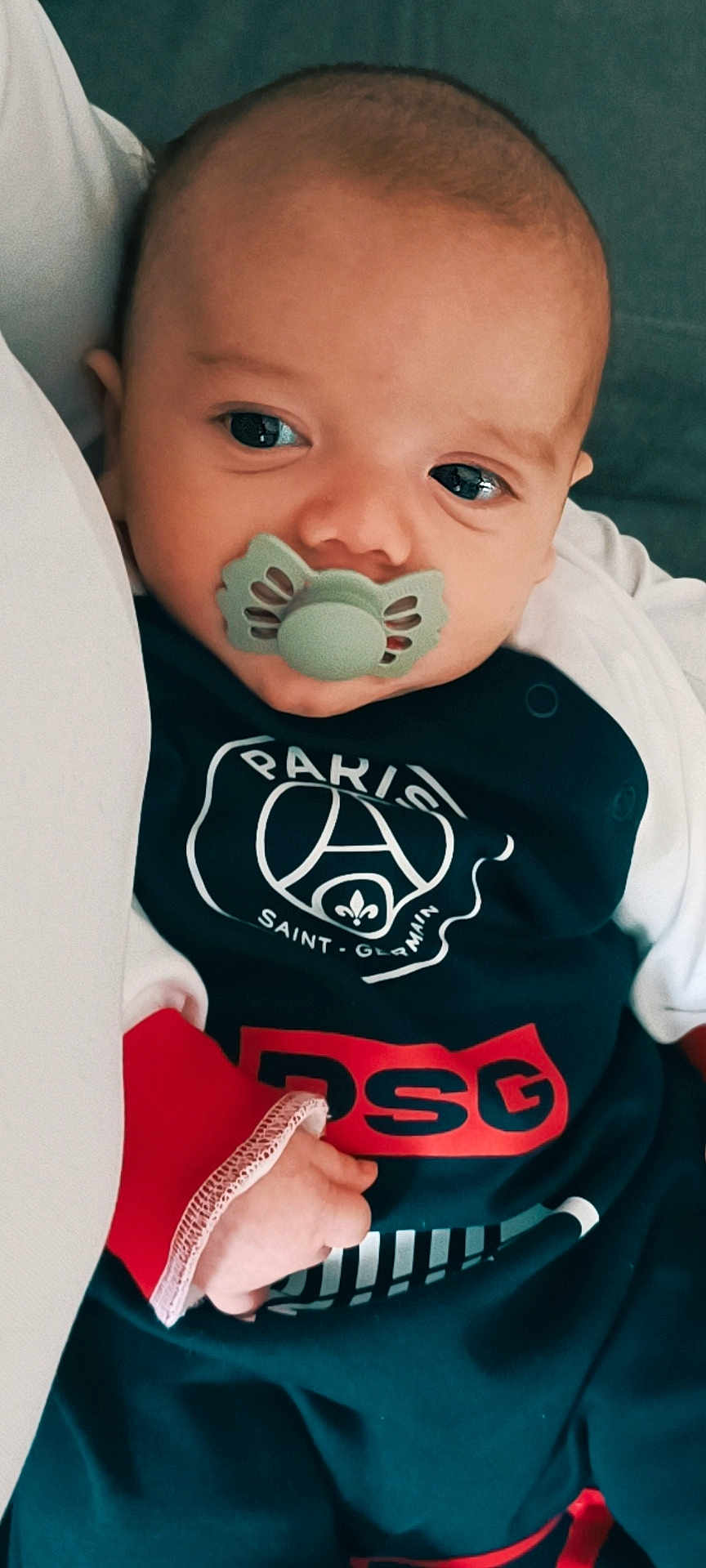 Cristiano participe au concours pour gagner de l'argent avec cette photo : baby, pacifier, infant, clothing, face, hand, portrait, close_up, indoor, child, cute, person, young, soft_lighting, expression, newborn, bed, sleepwear, logo, resting