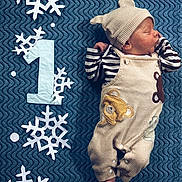 Roman is registered to the contest to win money with this photo: baby, newborn, sleeping, infant, blanket, bear_outfit, hat, striped_shirt, foot, hand, snowflake, paper_cutout, number_one, blue_background, cozy, cute, portrait, indoors, resting, child