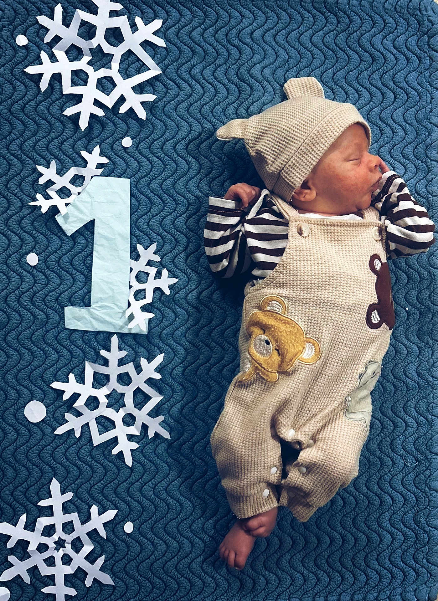 Roman is registered to the contest to win money with this photo: baby, newborn, sleeping, infant, blanket, bear_outfit, hat, striped_shirt, foot, hand, snowflake, paper_cutout, number_one, blue_background, cozy, cute, portrait, indoors, resting, child