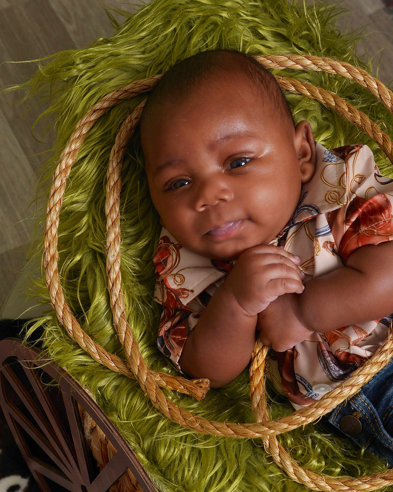 Ezekiel is registered to the contest to win money with this photo: baby, infant, child, face, hand, rope, green_rug, patterned_shirt, denim, clothing, cute, portrait, indoors, wooden_chair, skin, expression, closeup, soft_lighting, resting, curious