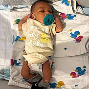 Ezekiel is registered to the contest to win money with this photo: baby, newborn, pacifier, onesie, sleeping, blanket, duck_pattern, infant, clothing, cute, resting, indoors, baby_sock, diaper, soft_fabric, child, peaceful, laying_down, toddler, nursery