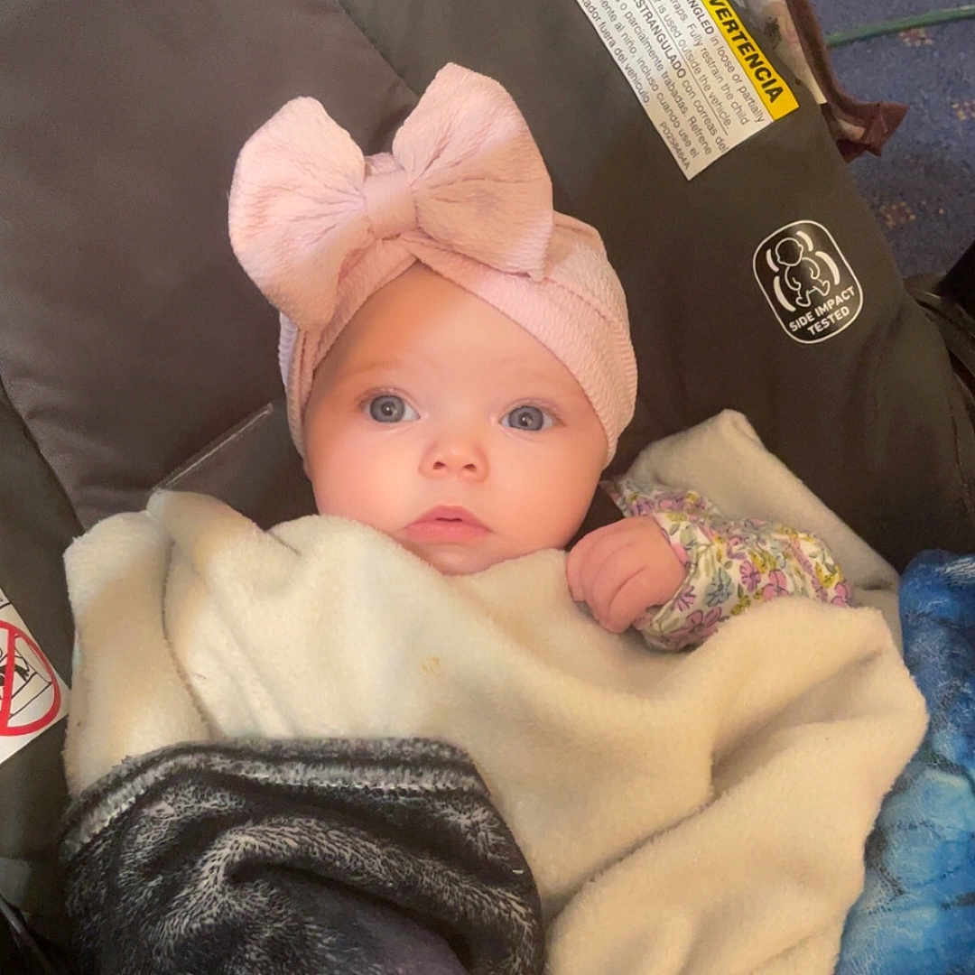 Stefanie Lynn is registered to the contest to win money with this photo: baby, infant, blanket, car_seat, headband, pink_bow, blue_eyes, indoor, cozy, clothing, person, child, portrait, cute, warm, soft_lighting, floor, fabric, wrapped, seated