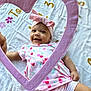 baby, infant, smiling, pink_bow, heart_frame, blanket, cute, child, patterned_clothing, happy, lying_down, headband, cherry_pattern, soft_texture, indoors, playful, bright, portrait, adorable, toddler