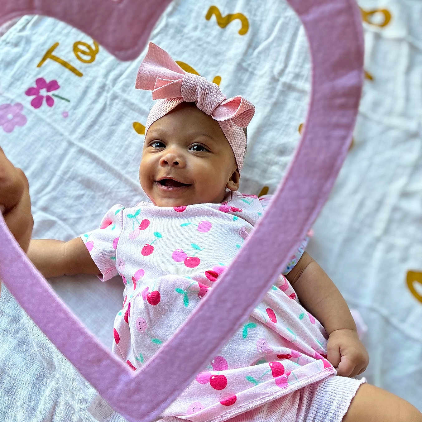 Amelia joined the competition — help win amazing prizes! adorable, baby, blanket, bright, cherry_pattern, child, cute, happy, headband, heart_frame, indoors, infant, lying_down, patterned_clothing, pink_bow, playful, portrait, smiling, soft_texture, toddler