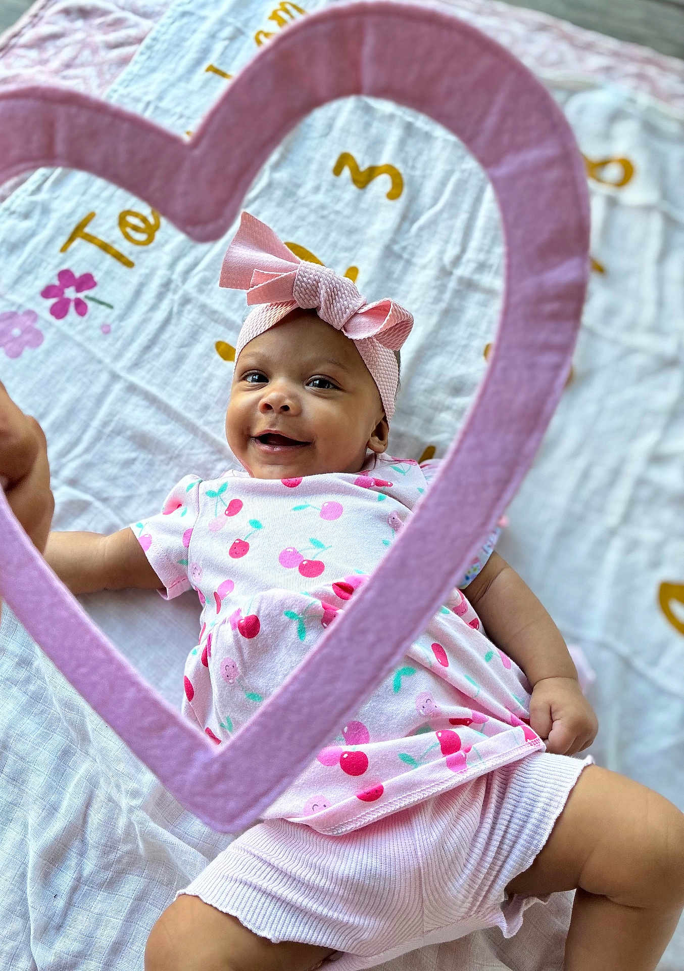 Amelia joined the competition — help win amazing prizes! baby, infant, smiling, pink_bow, heart_frame, blanket, cute, child, patterned_clothing, happy, lying_down, headband, cherry_pattern, soft_texture, indoors, playful, bright, portrait, adorable, toddler