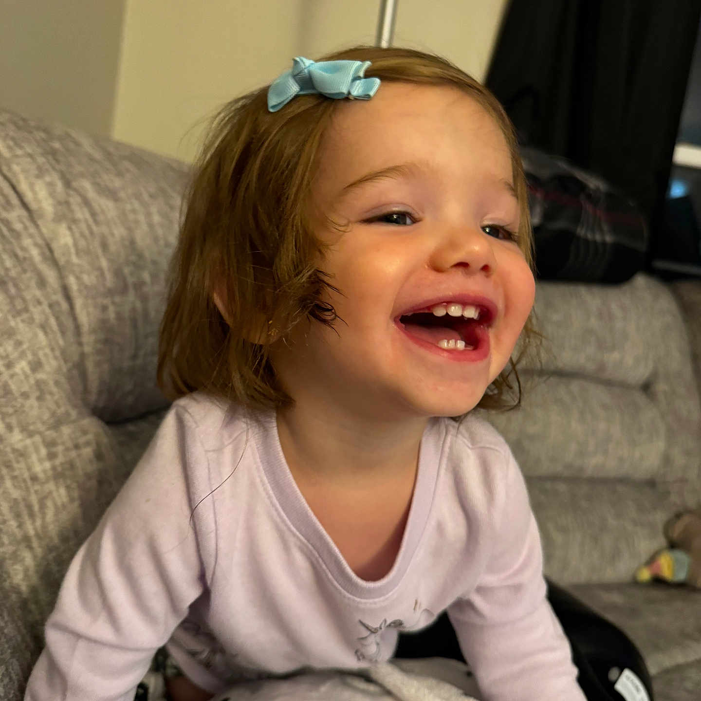 Elliana is registered to the contest to win money with this photo: toddler, child, smiling, laughing, blue_bow, hair_accessory, couch, blanket, indoor, cozy, happy, person, face, clothing, home, living_room, cute, young_child, fun, portrait