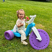 Elliana is registered to the contest to win money with this photo: toddler, smiling, tricycle, toy, grass, outdoor, child, play, watermelon, greenery, person, trees, happy, footwear, clothing, nature, park, summer, daylight, cute