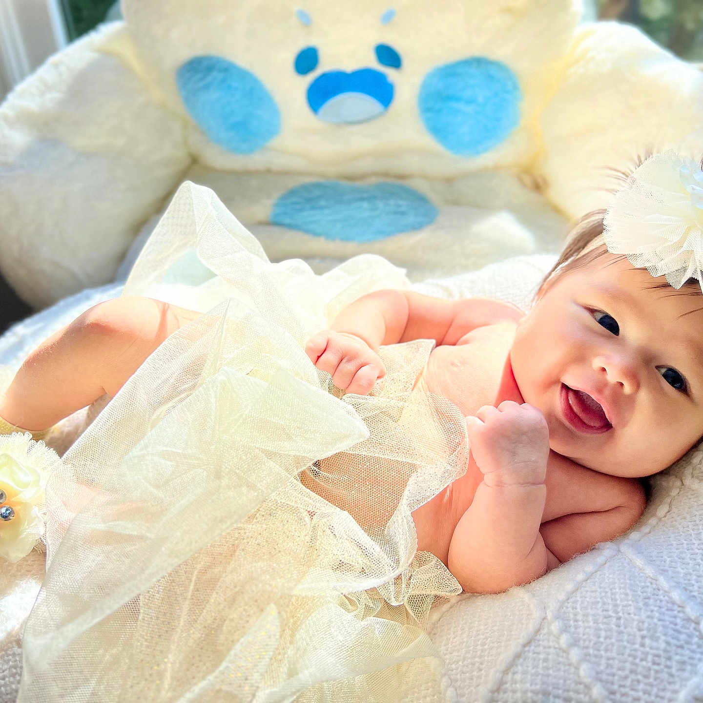 Wrynn is registered to the contest to win money with this photo: ankle_band, baby, baby_clothing, child, cozy, cute, face, happy, headband, indoor, infant, natural_light, plush_chair, portrait, resting, smiling, soft_texture, tulle_skirt, white_blanket, window