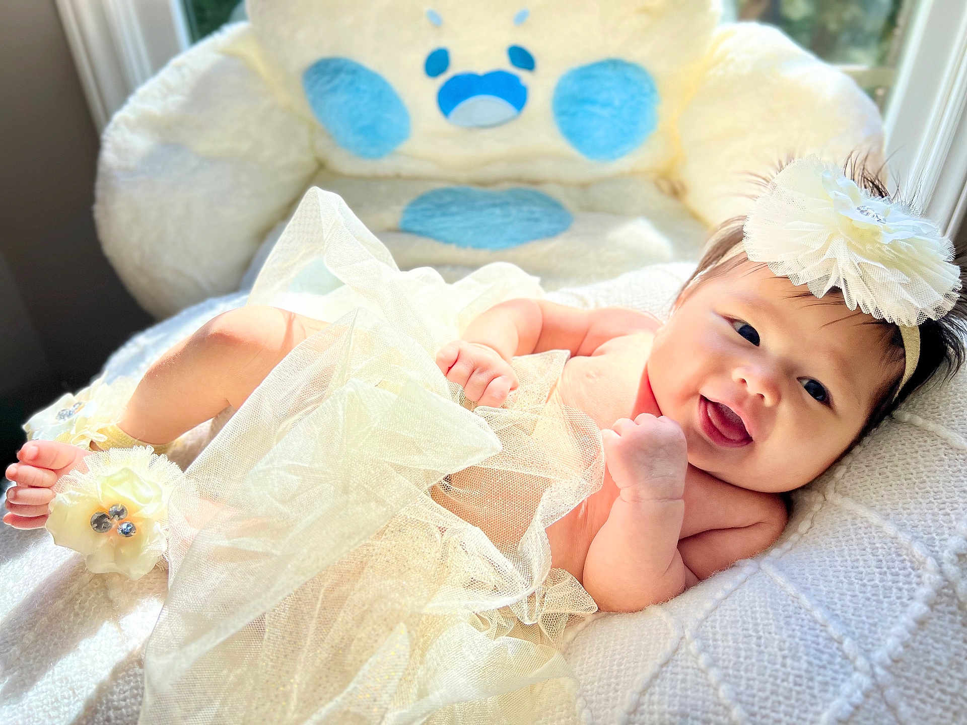 Wrynn is registered to the contest to win money with this photo: baby, smiling, infant, tulle_skirt, headband, ankle_band, plush_chair, white_blanket, natural_light, window, cozy, soft_texture, cute, happy, indoor, portrait, baby_clothing, child, face, resting
