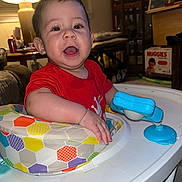Kaine is registered to the contest to win money with this photo: baby, child, walker, toy, red_shirt, smiling, indoor, lamp, furniture, table, diapers, huggies, person, happy, face, hand, living_room, colorful, play, infant