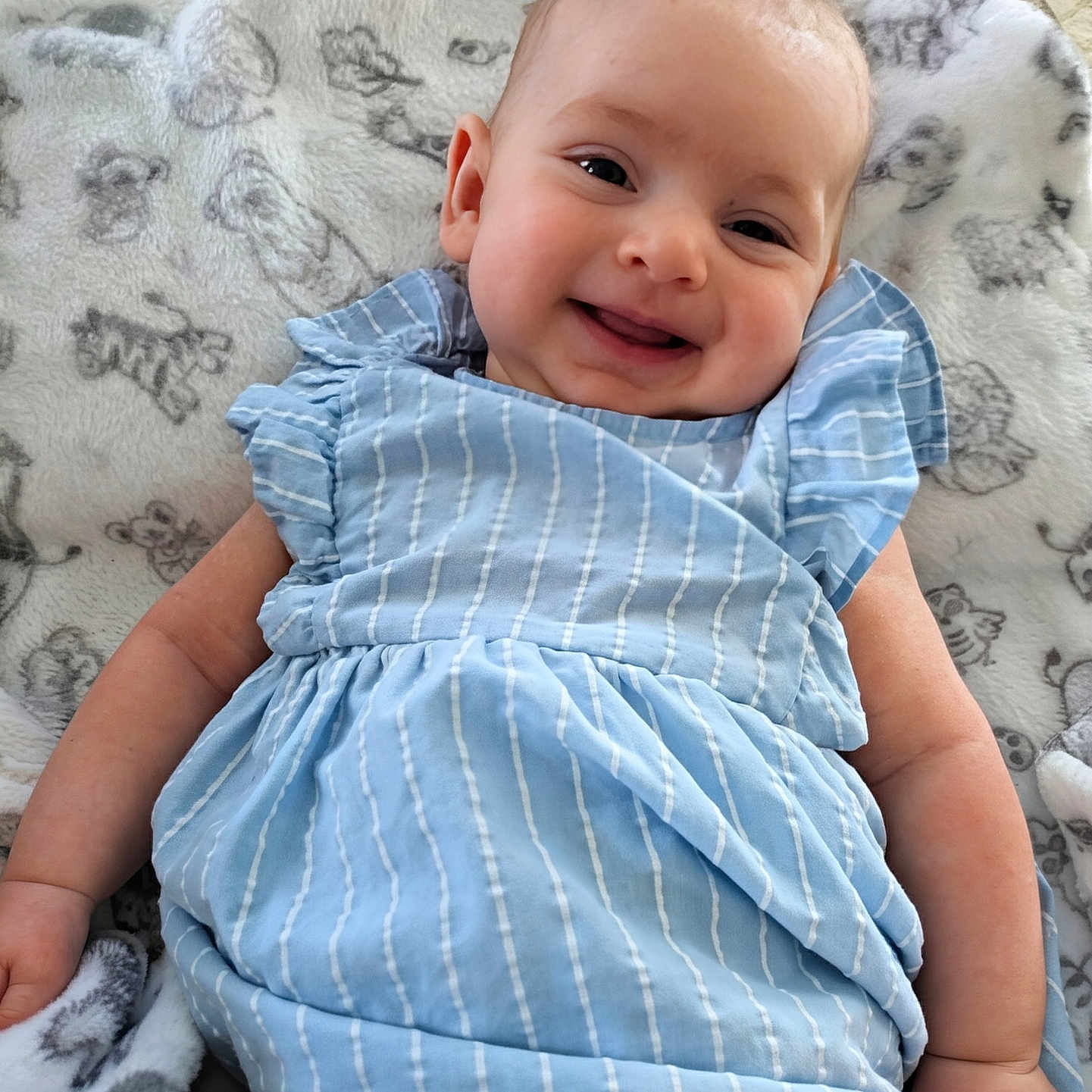 Amelia is registered to the contest to win money with this photo: baby, smiling, blue_dress, blanket, animal_pattern, infant, cute, happy, child, lying_down, soft_texture, cozy, portrait, skin, arm, head, face, indoors, young_child, clothing