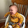Eli is registered to the contest to win money with this photo: baby, child, smiling, happy, onesie, yellow_clothing, striped_clothing, baby_seat, high_chair, wooden_chair, indoor, infant, cute, person, seatbelt, furniture, face, hands, feet, playful