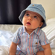 Alexander is registered to the contest to win money with this photo: baby, bed, child, clothing, curious, cute, denim, expression, feet, hands, hat, indoors, infant, looking_up, person, portrait, sitting, skin, striped_shirt, white_bed