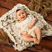 Hope a rejoint le concours — aidez-le/la à gagner de superbes lots ! baby, infant, smiling, floral_blanket, headband, lace_dress, barefeet, toes, wooden_floor, pampas_grass, ferns, rustic, cozy, portrait, studio_props, cute, happy, lying_down, blanket, hands