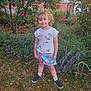 child, smiling, garden, flowers, greenery, tree, grass, shirt, skirt, socks, shoes, unicorn, flamingo, outdoor, nature, plants, daylight, person, happy, cute
