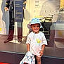 blanket, cartoon_print, child, clothing, display, exhibit, floor, footwear, happy, hat, history, indoor, mannequin, museum, person, red_floor, smiling, toddler, tshirt, young_child